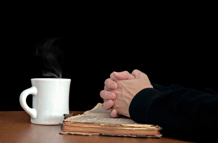 Photo of woman's hands clasped in prayer upon an open bible